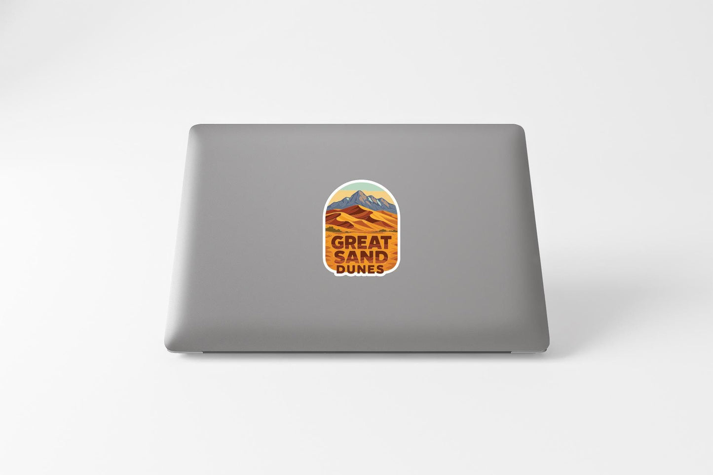 A sticker on the back of a laptop with the text "GREAT SAND DUNES" printed on it.