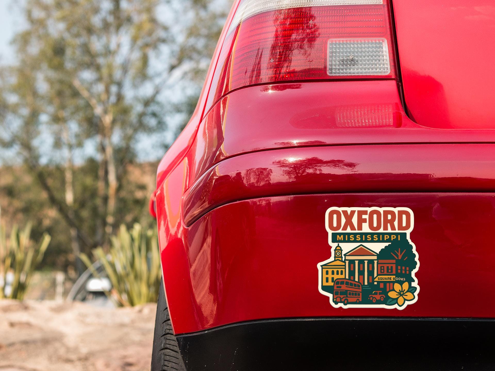 the rear end of a red car with a sticker on the back window that says "Oxford Mississippi".