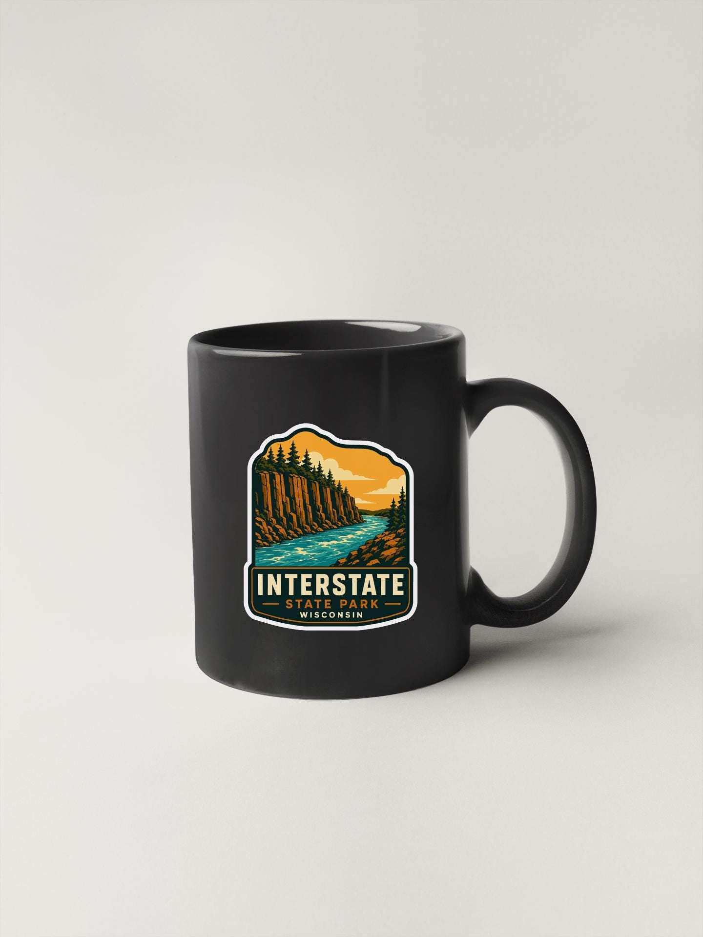 A black coffee mug with a graphic design depicting a scenic landscape with a river and mountains.
