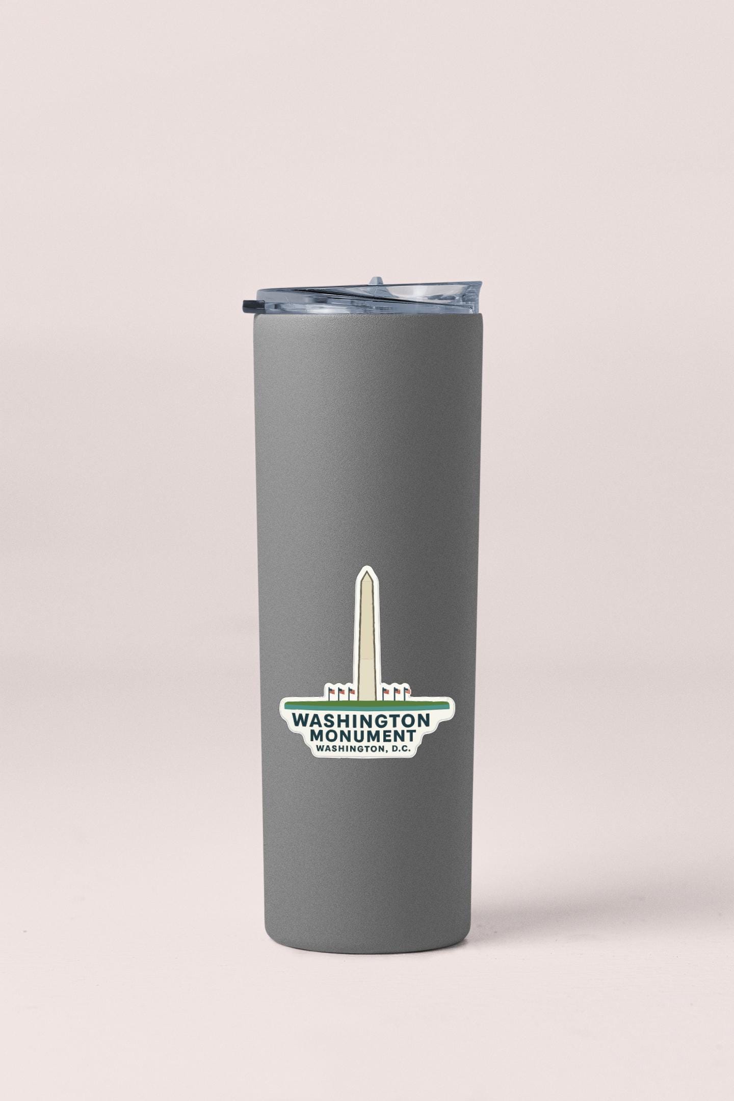 A gray insulated tumbler with a lid and a sticker featuring the Washington Monument logo.