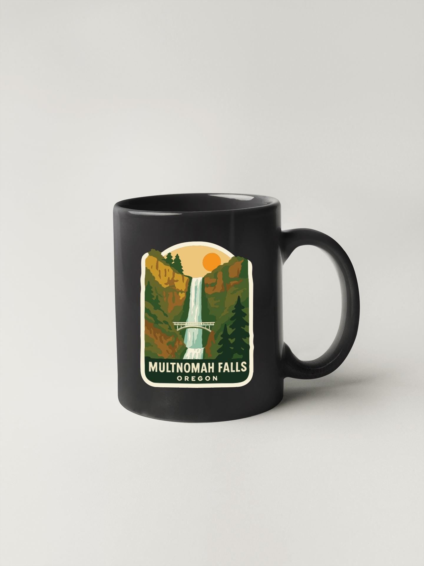 A black coffee mug with a graphic design depicting the scenic falls of Multnomah Falls in Oregon.