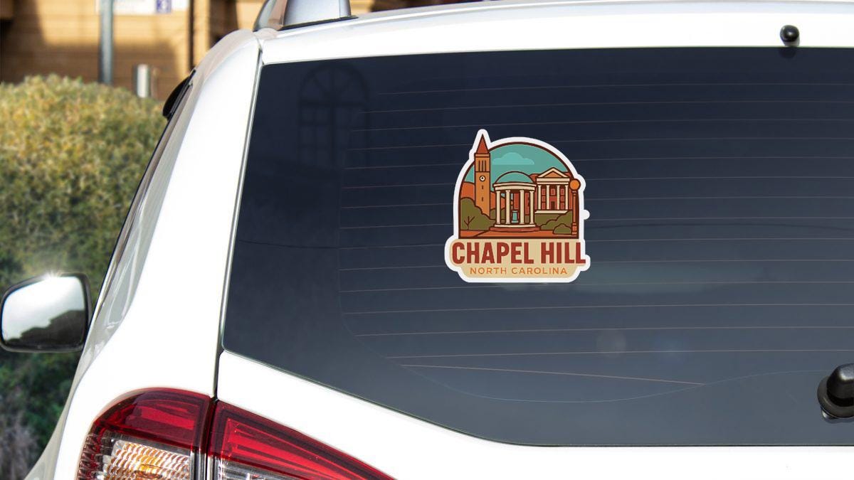 A sticker on the rear window of a white vehicle, depicting a building with a dome and a clock tower, representing Chapel Hill, North Carolina.