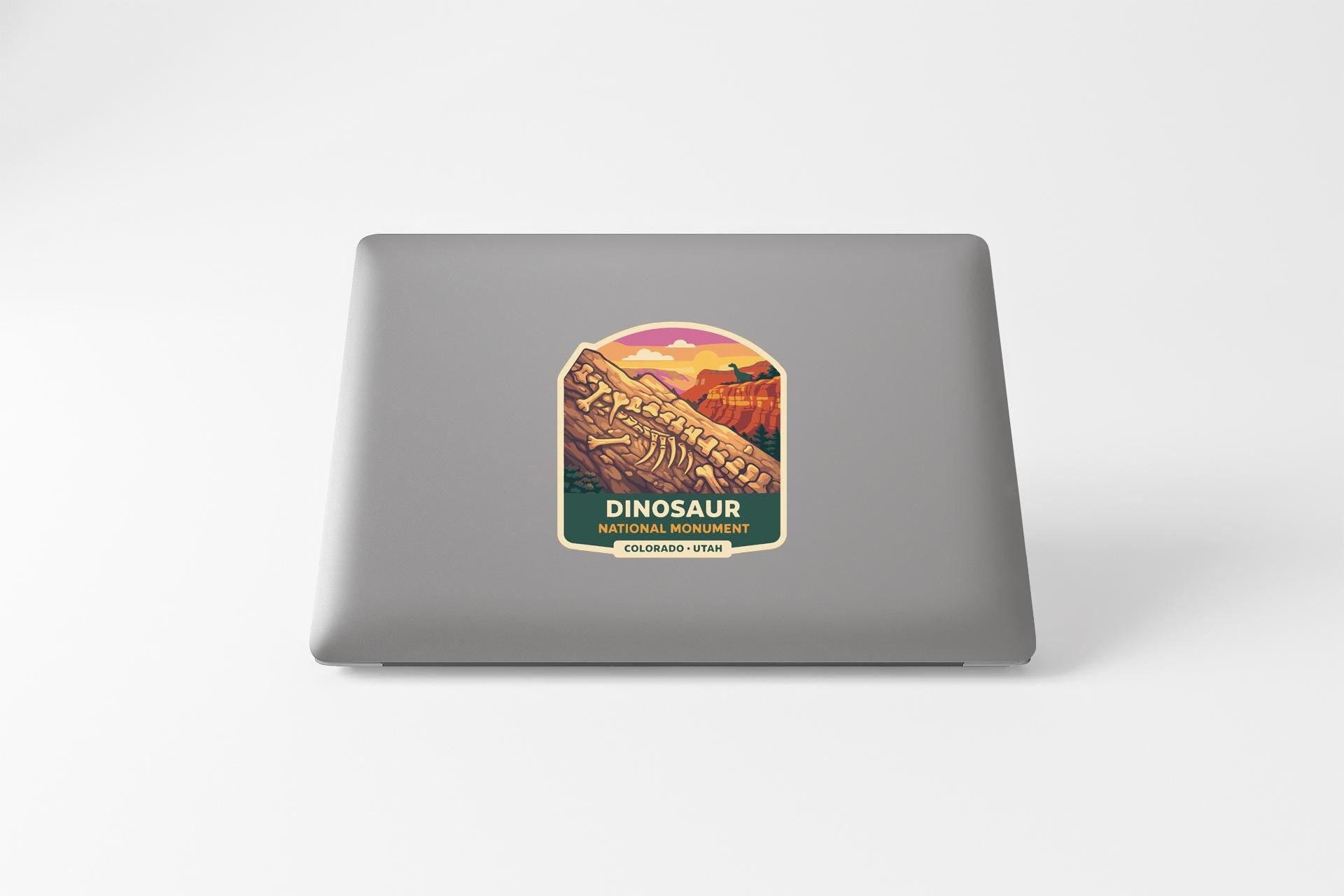 A sticker on the back of a laptop, depicting a scenic landscape with mountains and a dinosaur.