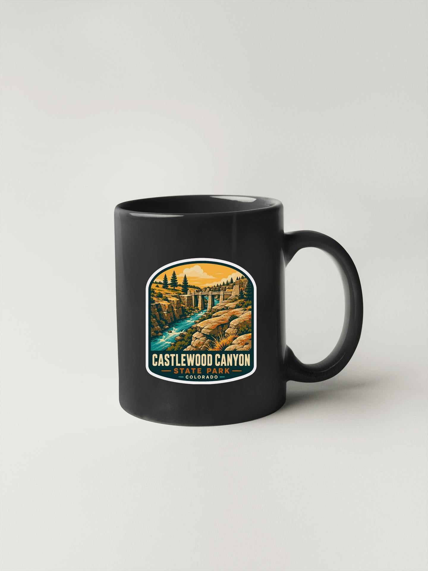 A black coffee mug with a graphic design depicting a scenic landscape, including a river, bridge, and mountains.