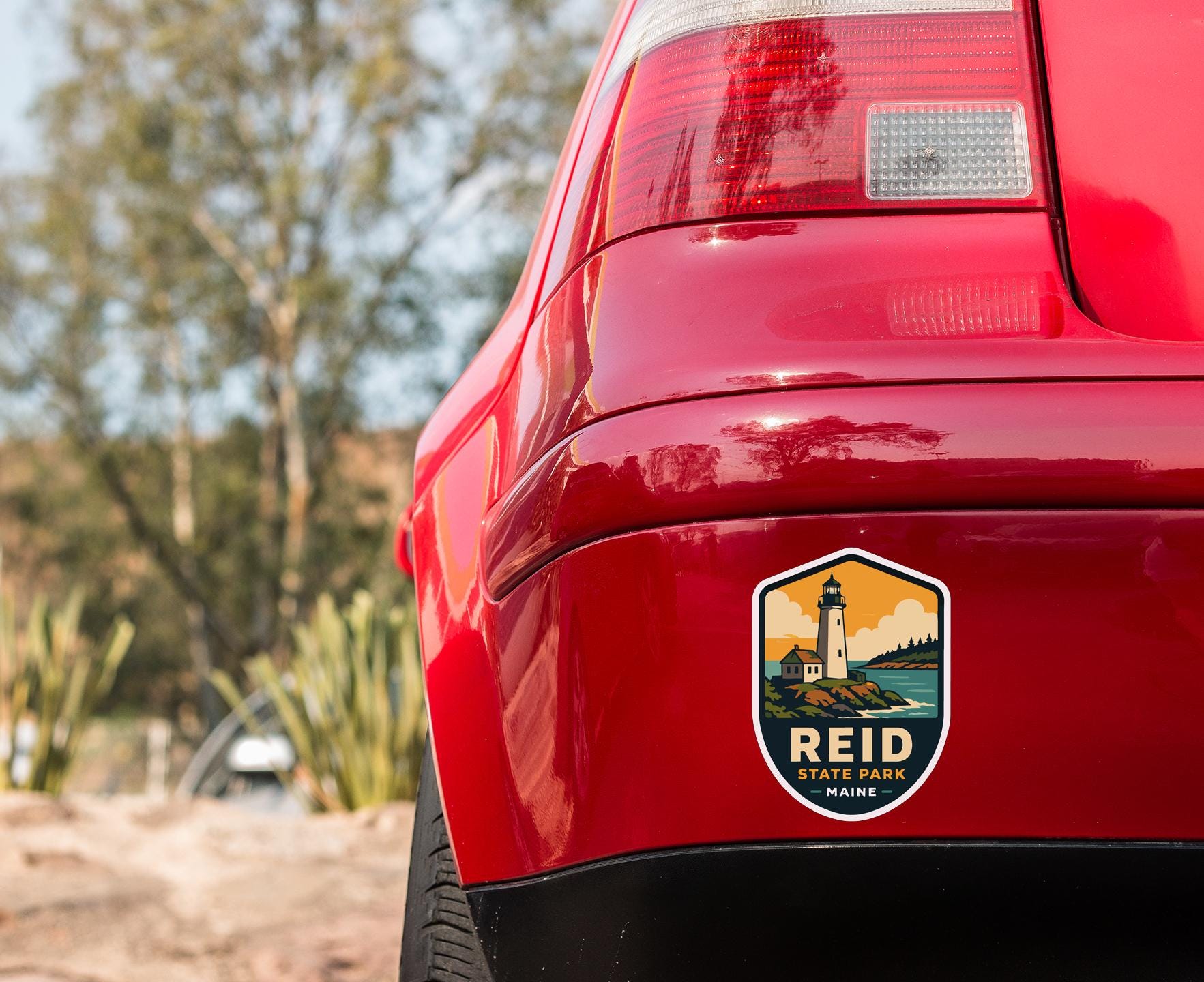 the rear end of a red car with a sticker on the back window that says " Reid State Park Maine".