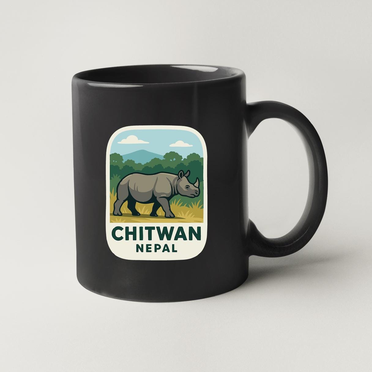 A black coffee mug with a label that features an illustration of a rhinoceros and the text "CHITWAN NEPAL".