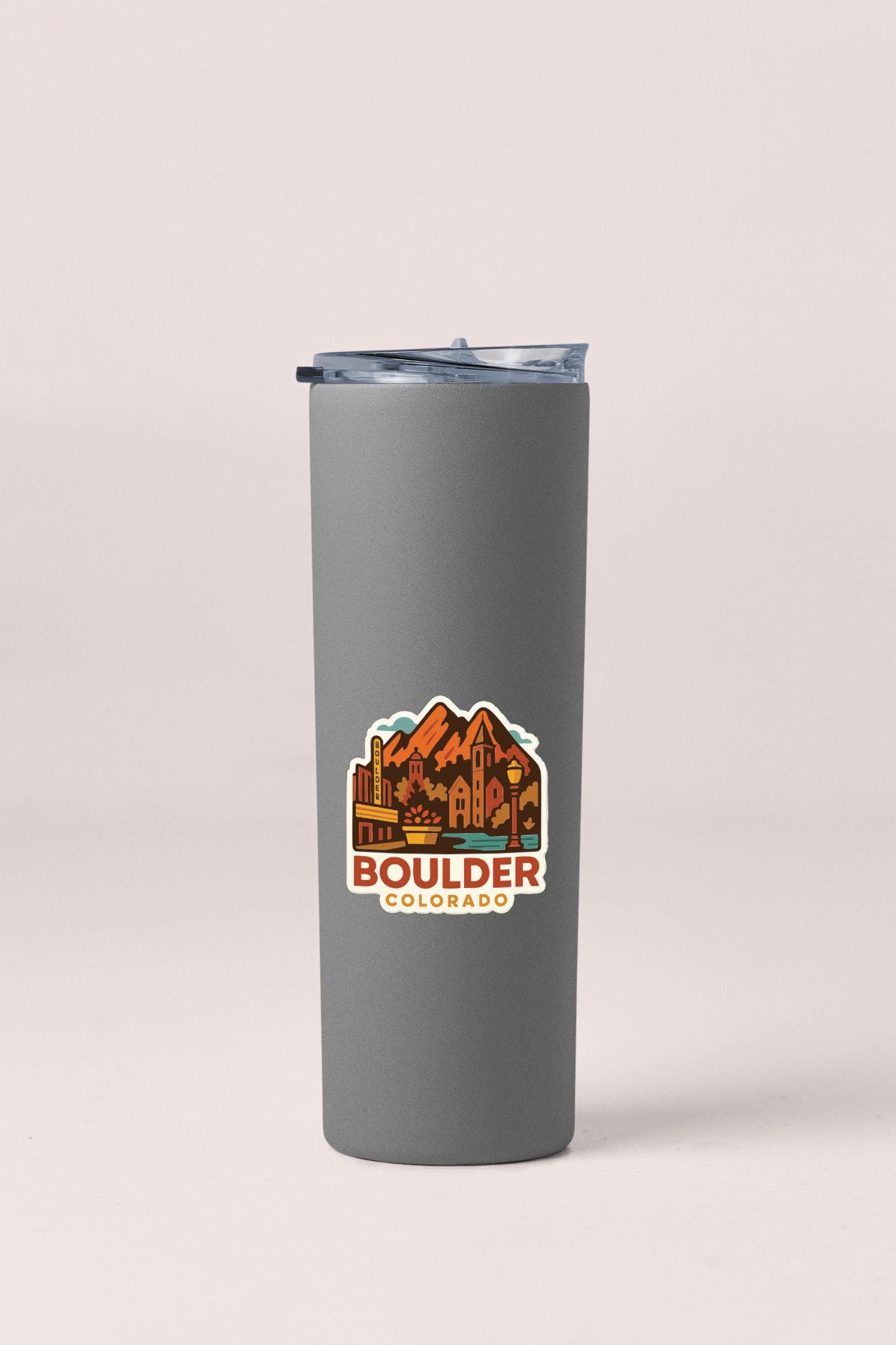 A gray insulated tumbler with a lid and a sticker depicting the city of Boulder, Colorado.
