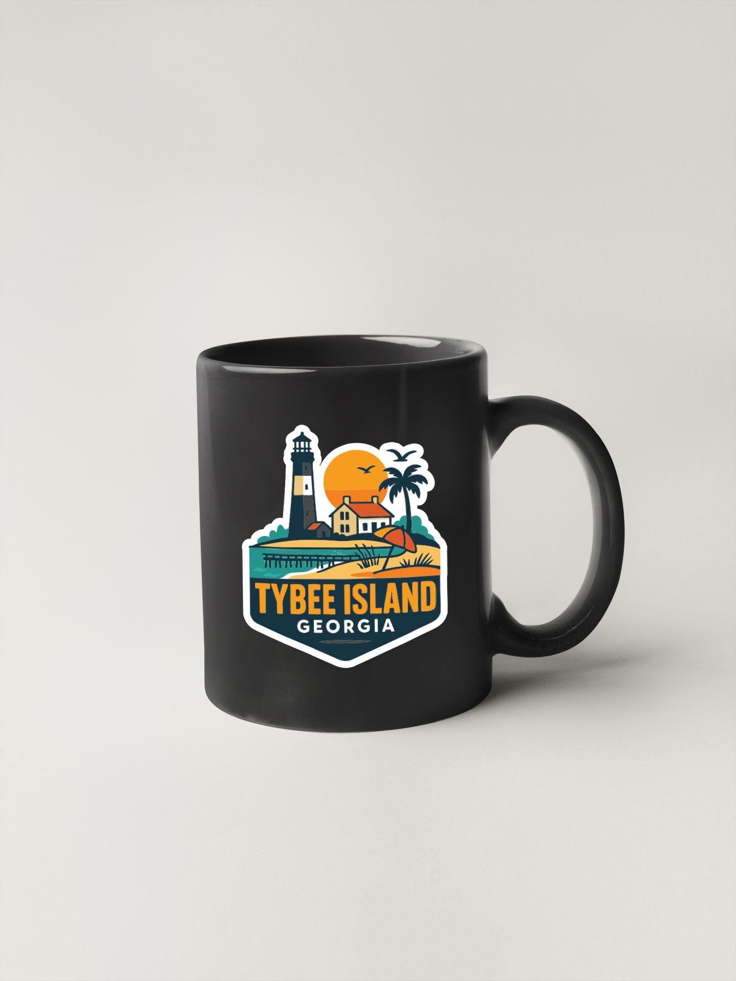 A black coffee mug with a colorful graphic depicting a lighthouse, palm trees, and a sunset on Tybee Island, Georgia.