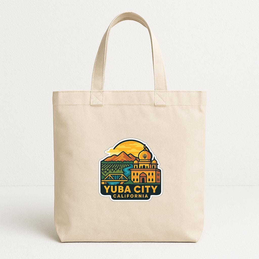 A beige tote bag with a graphic design featuring a city skyline and mountains, along with the text "YUBA CITY CALIFORNIA".
