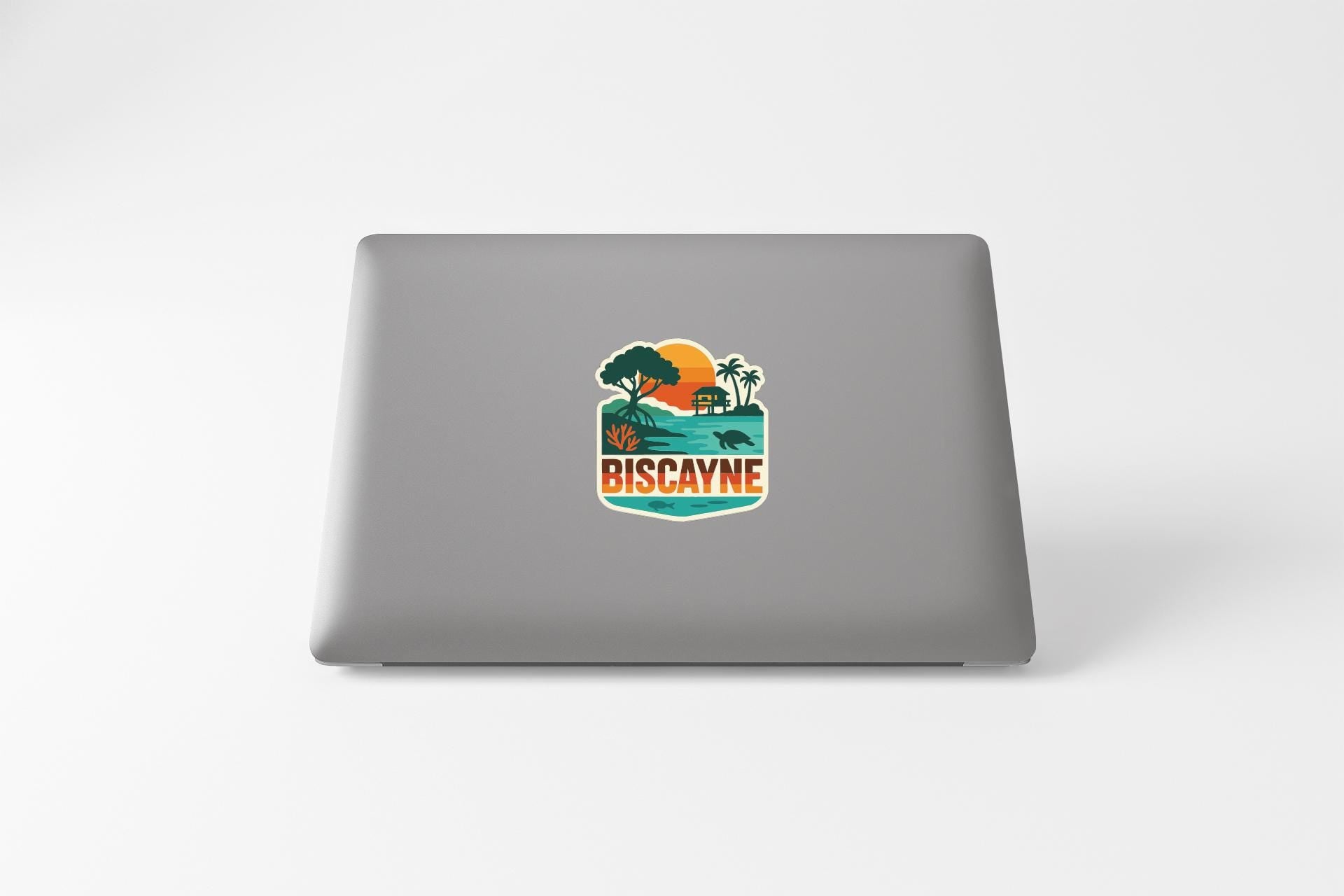 a sticker with a tropical landscape and the word "BISCAYNE" on the back of a laptop.
