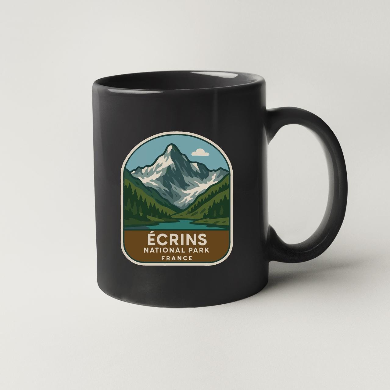 A black coffee mug with a mountain landscape and text that says "ÉCRINS NATIONAL PARK FRANCE".