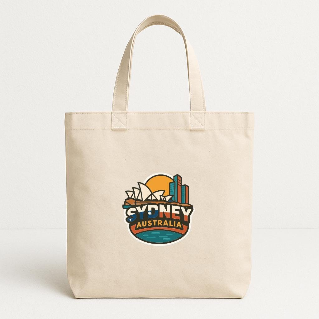 A beige tote bag with a graphic design featuring the text "SYDNEY AUSTRALIA" and a stylized representation of the Sydney skyline.