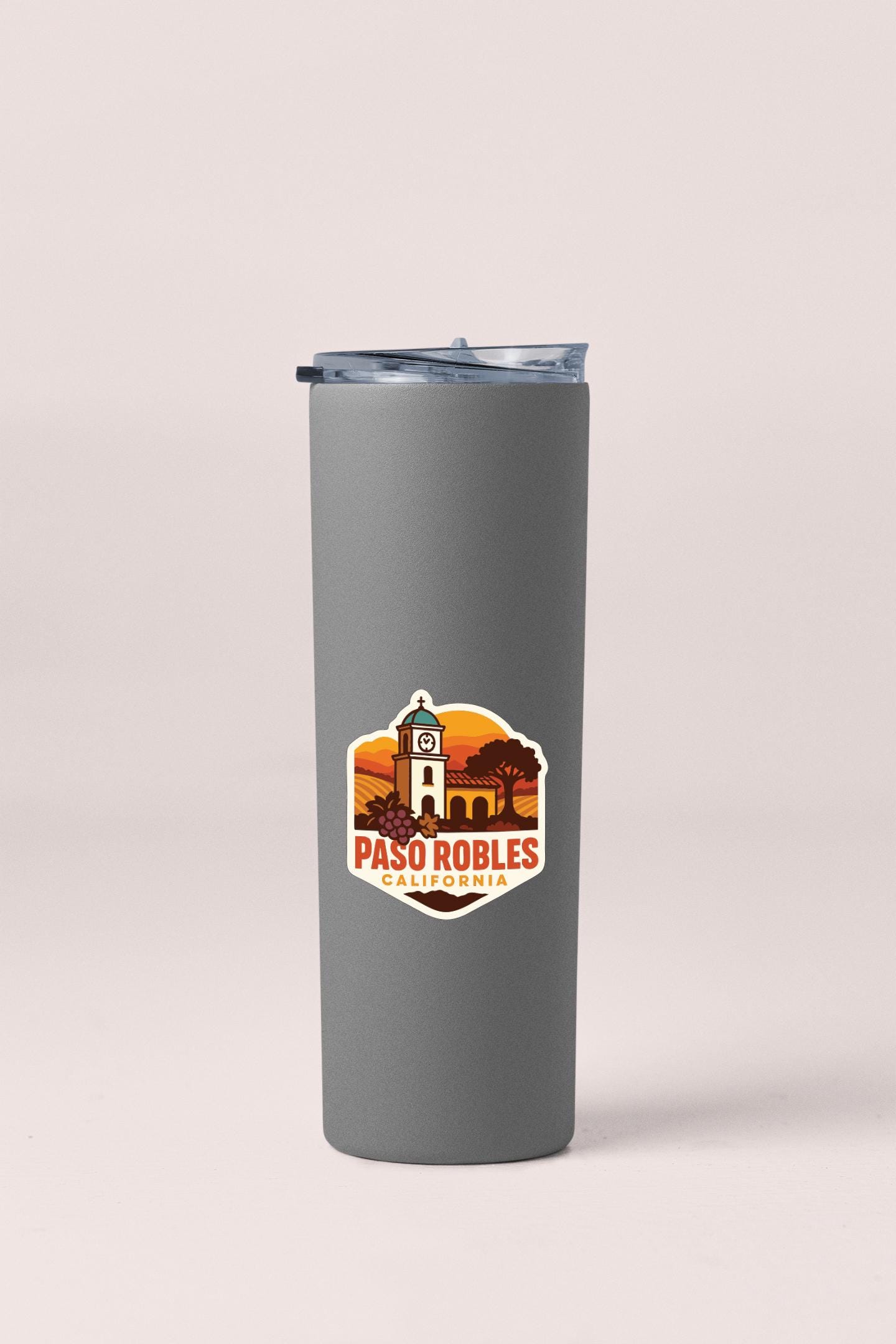 A gray insulated tumbler with a lid and a sticker featuring a graphic of a building and the text "PASO ROBLES" printed on it.