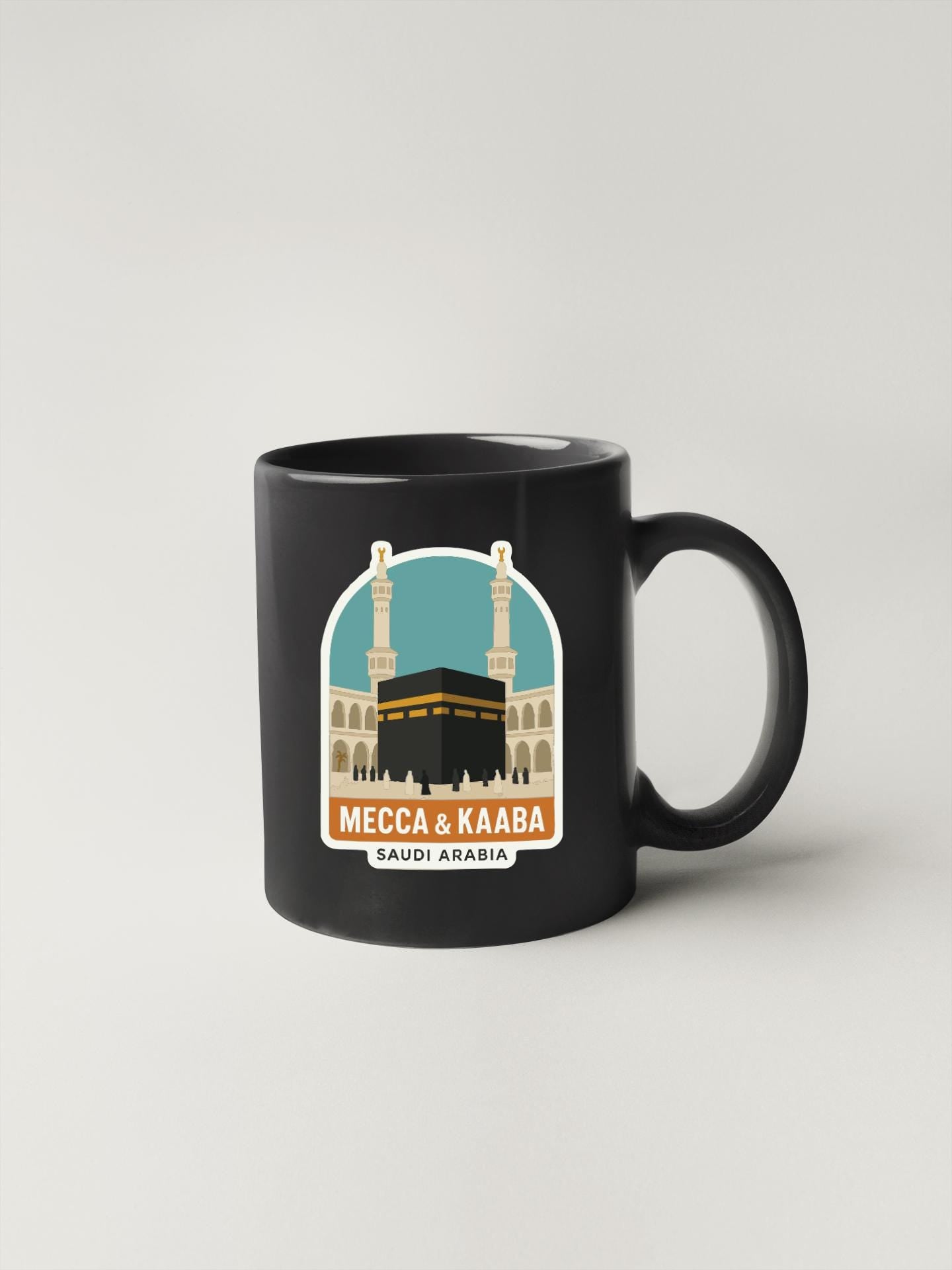 A black coffee mug with a graphic design depicting the Kaaba and the Masjid of Mecca, which is a significant religious site in Saudi Arabia.