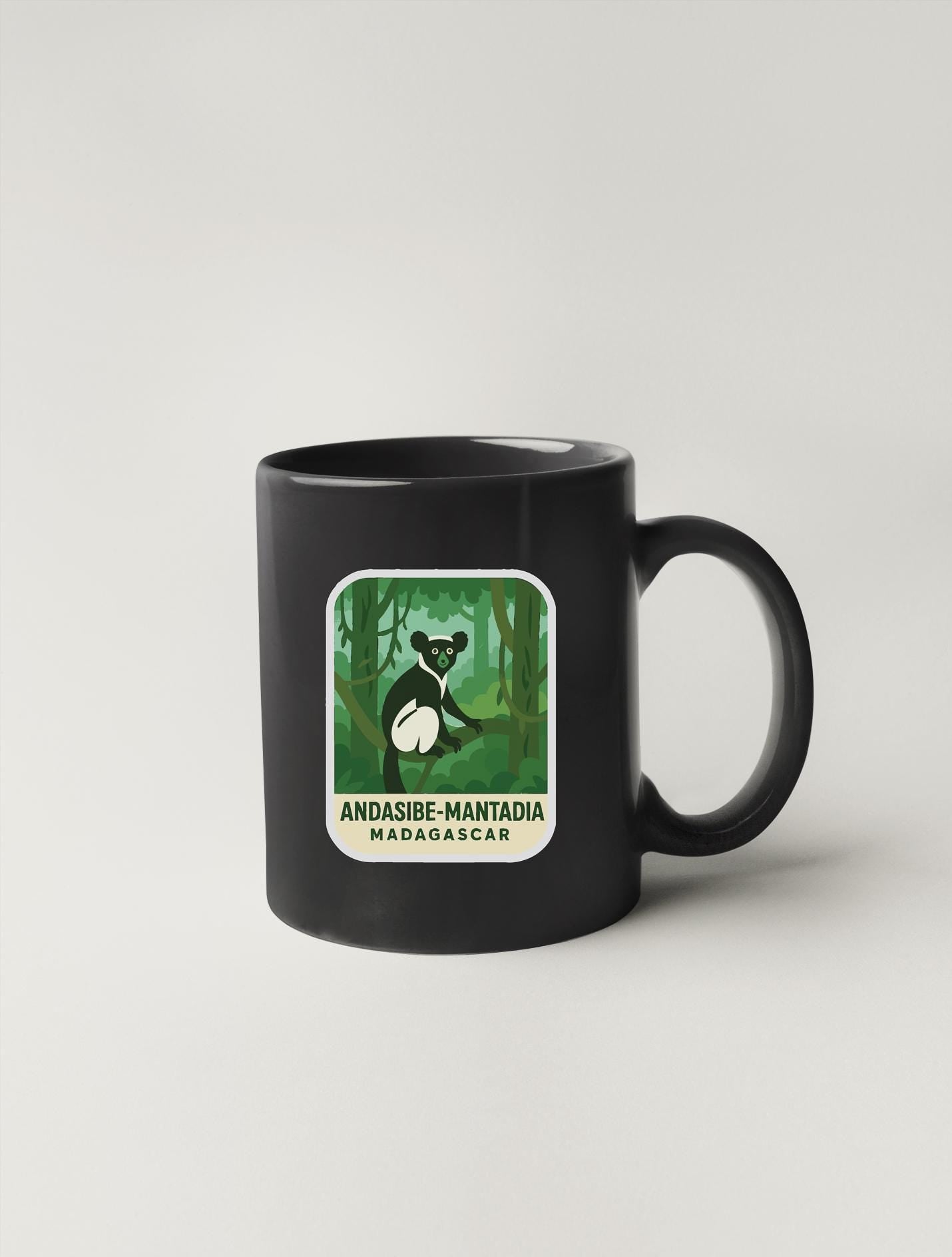 A black coffee mug with a green and white sticker depicting a lemur in a forest setting.