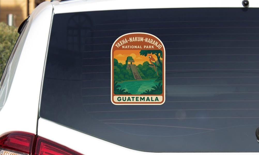 A sticker on the rear window of a car, depicting a scenic landscape with a waterfall and a tropical forest, with the text "XAYA-KAMUK-NARANO NATIONAL PARK GUATEMALA".