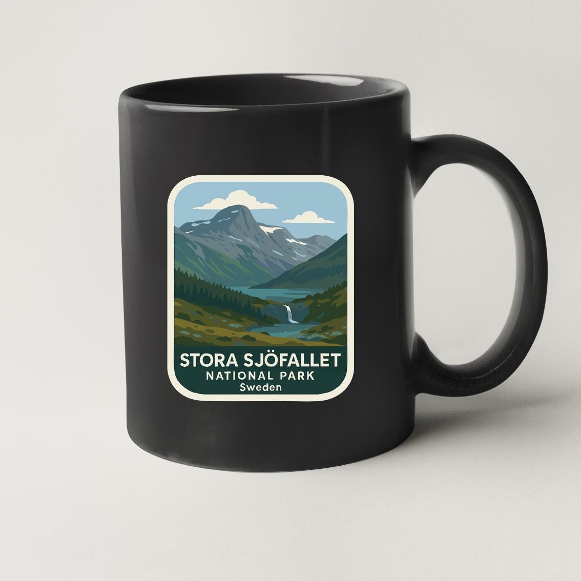 A black coffee mug with a sticker depicting a scenic mountain landscape.