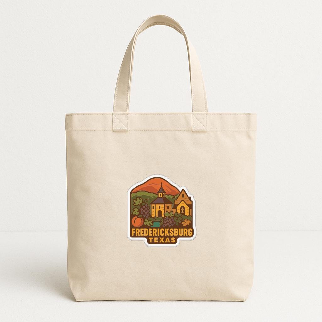A beige tote bag with a printed design depicting a scenic view of Fredericksburg, Texas.