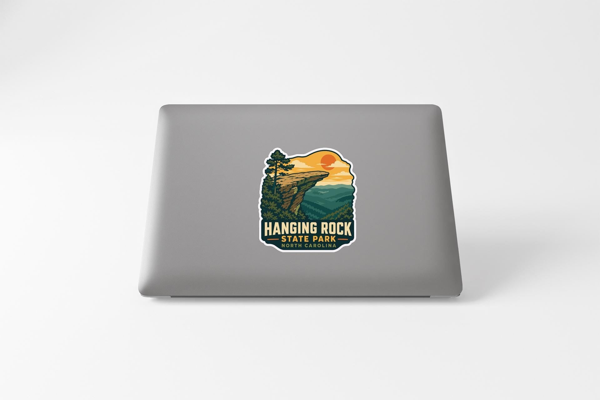 A sticker on the back of a laptop, depicting a scenic landscape with a cliff and a sunset.