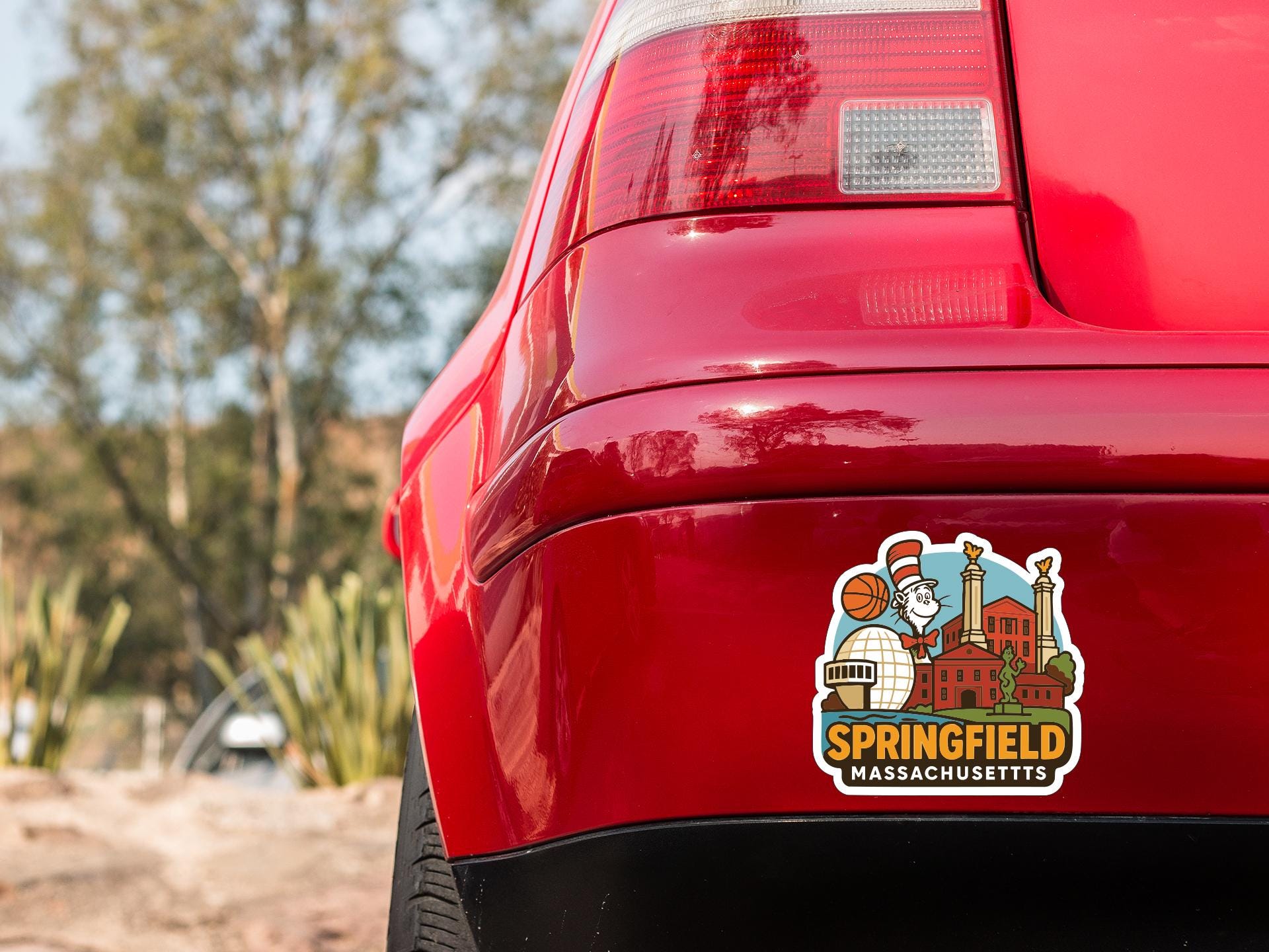 the rear end of a red car with a sticker on the trunk that features an illustration of a city skyline and the text "Springfield, Massachusetts".