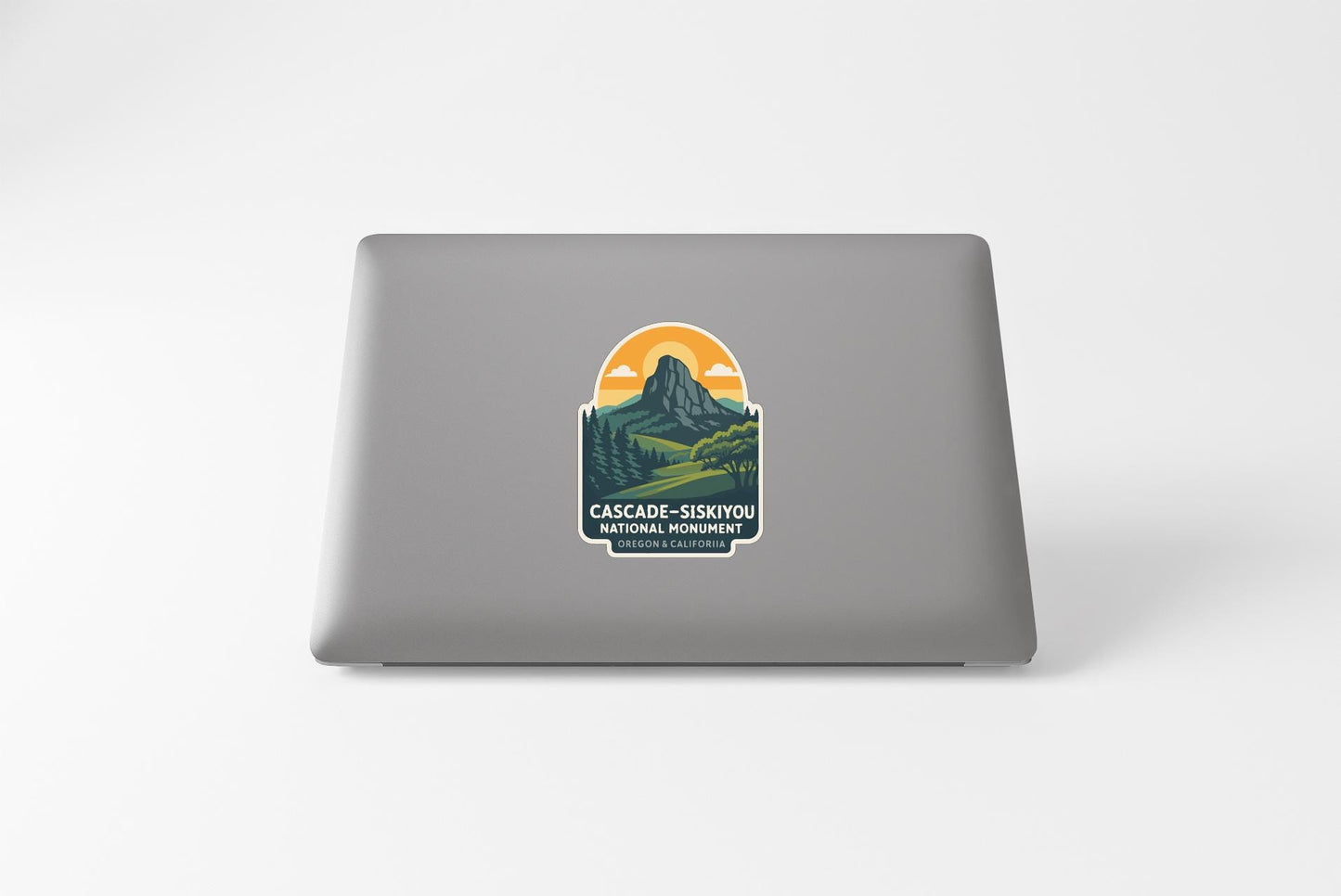a sticker on the back of a laptop that displays a mountain landscape with a sunrise or sunset in the background.
