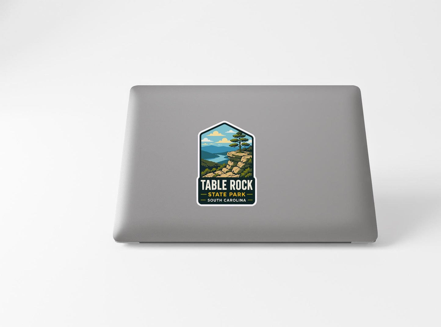 A sticker on the back of a laptop, depicting a scenic landscape with mountains, trees, and a body of water.
