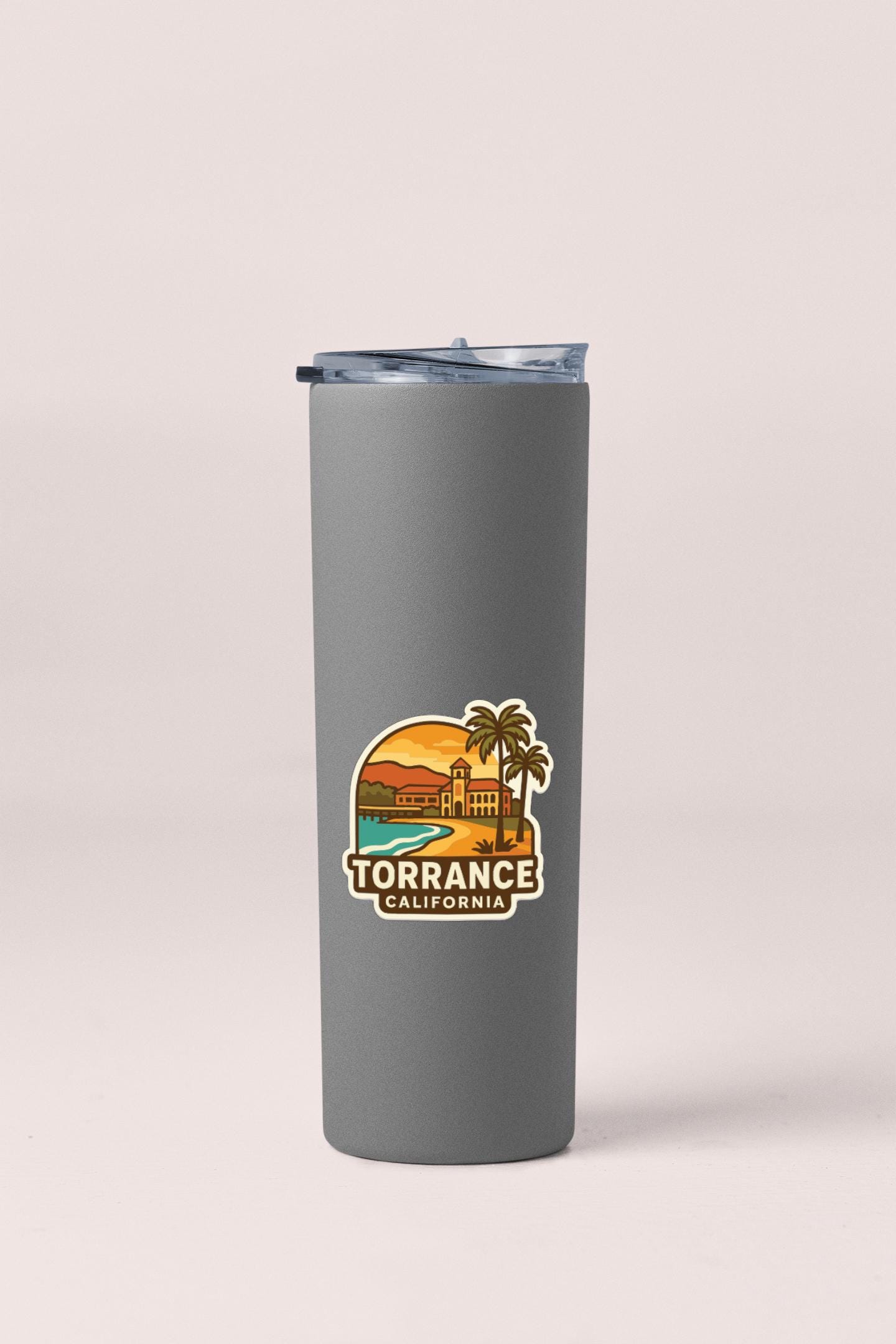 A gray insulated tumbler with a lid and a sticker depicting a beach scene with a palm tree and a building.