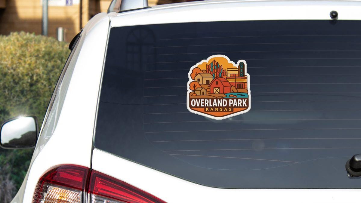 A sticker on the rear window of a white vehicle, displaying an illustration of a park with various buildings and elements.