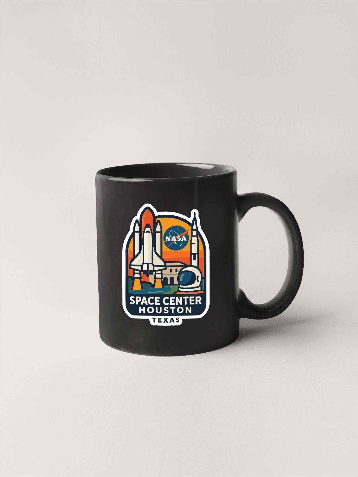 A black coffee mug with a graphic design featuring a space shuttle and the text "SPACE CENTER HOUSTON TEXAS" printed on it.