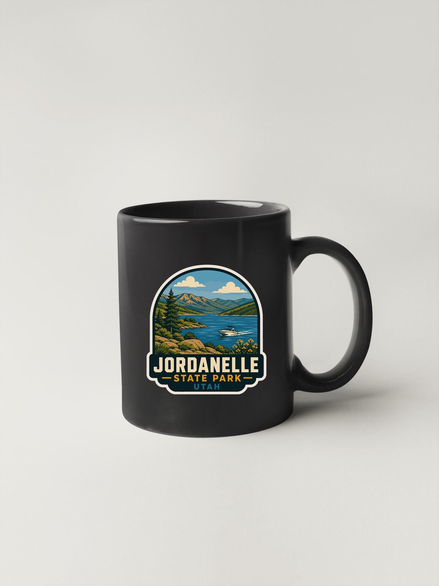 A black coffee mug with a graphic design depicting a scenic landscape, including mountains, a lake, and a forest.