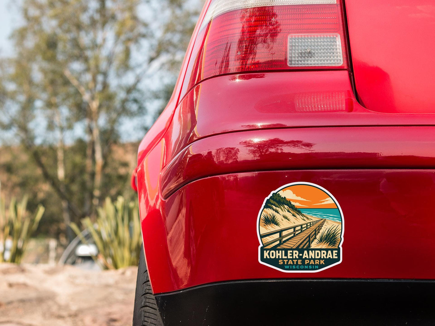 the rear end of a red car with a sticker on the back window that says "Kohler-Andrae State Park, Wisconsin".