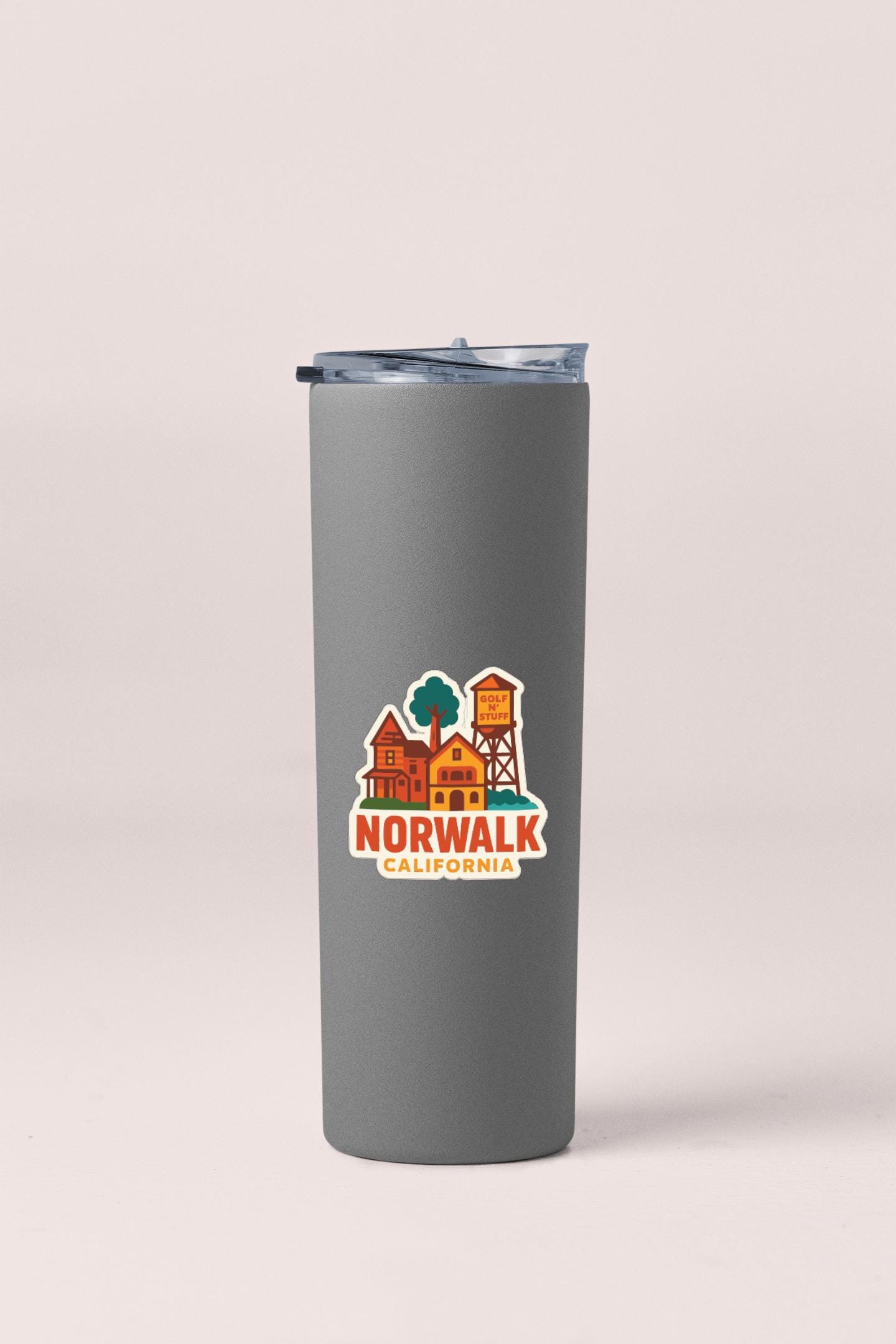 A gray insulated tumbler with a lid and a sticker featuring a graphic of a town or village.