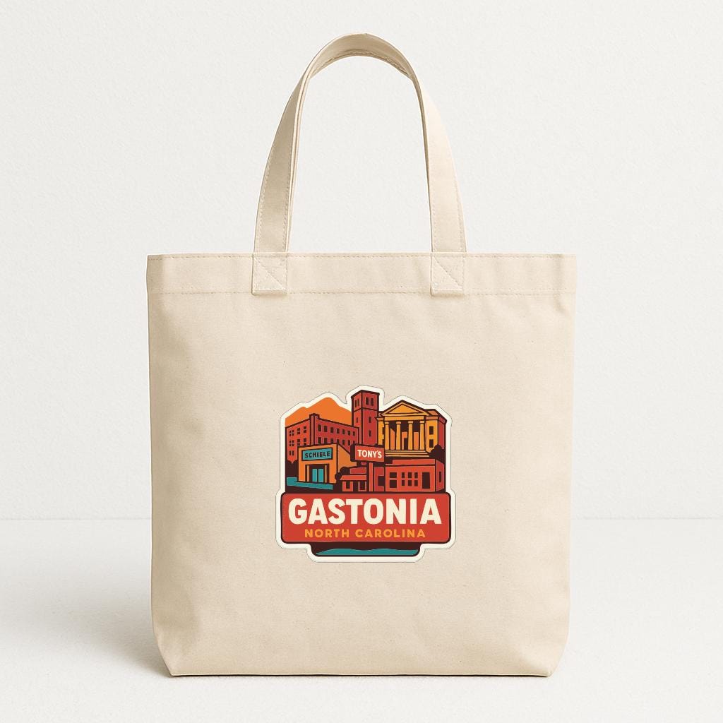 A beige tote bag with a graphic design featuring a cityscape and the text "GASTONIA NORTH CALIFORNIA".