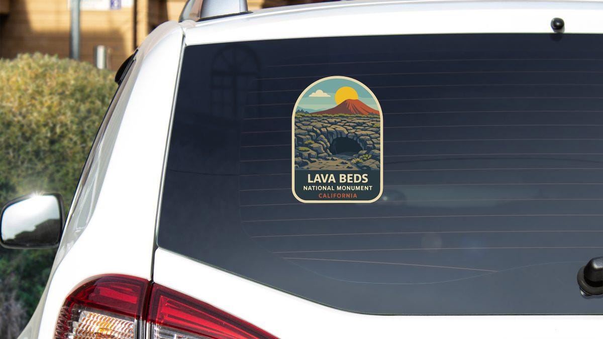 the rear window of a white car with a sticker on it, featuring a scenic landscape with a mountain and a volcano.