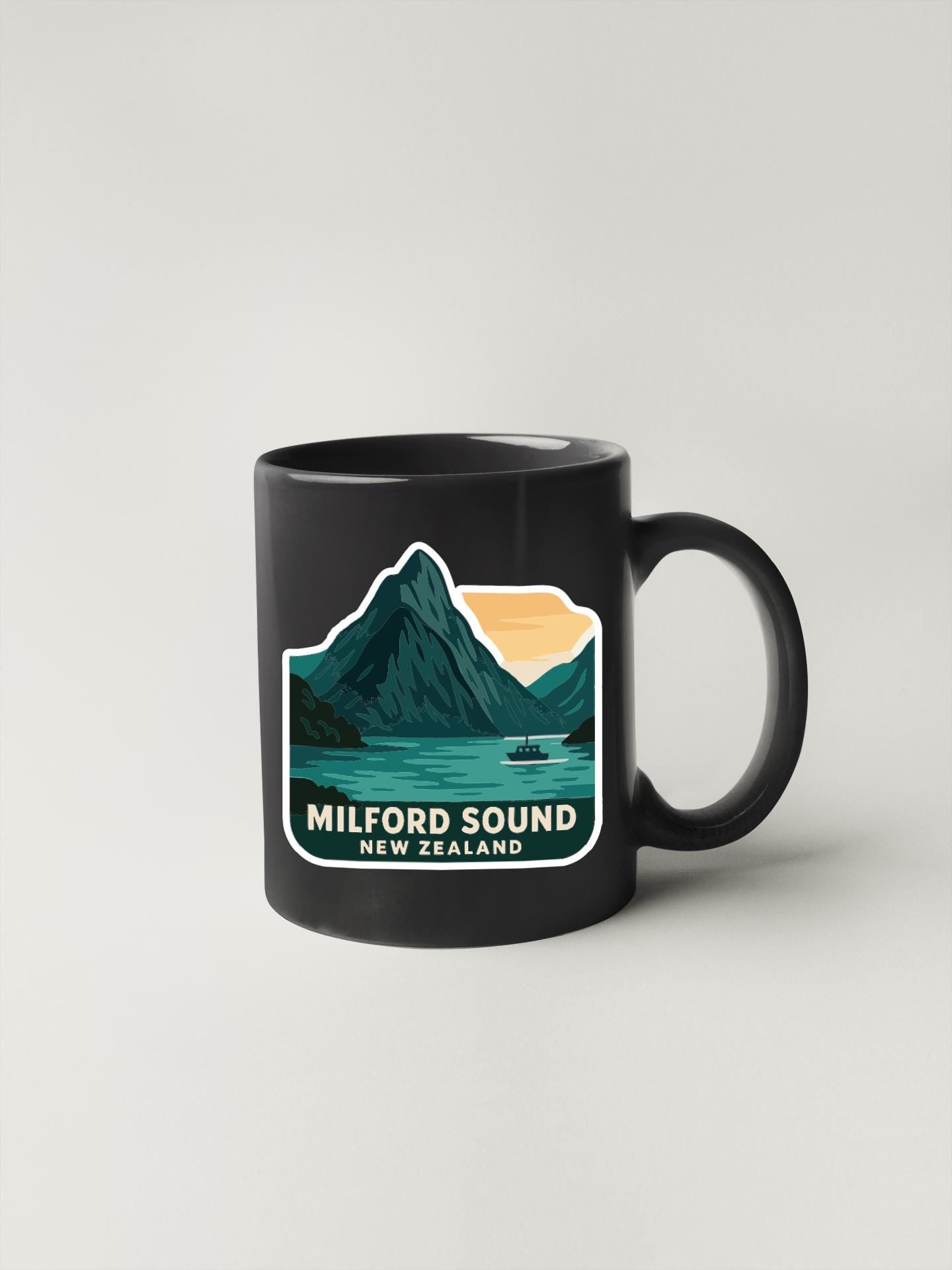 A black coffee mug with a graphic design depicting Milford Sound, a famous landmark in New Zealand.