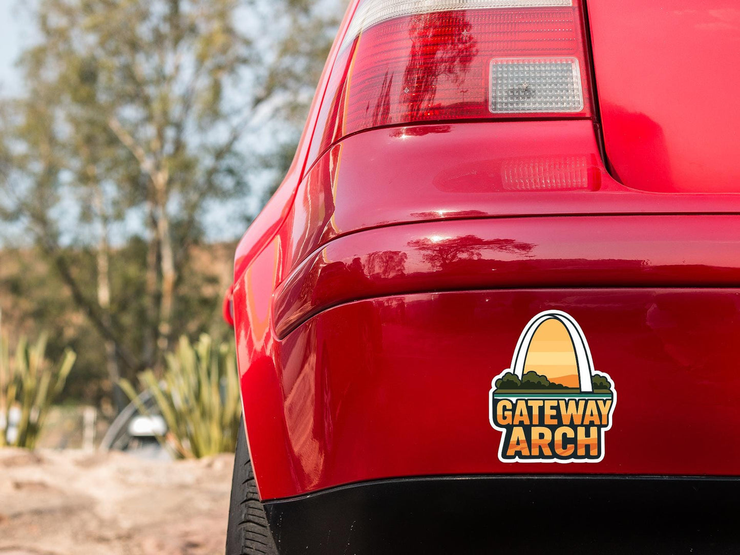 the rear end of a red car with a sticker on it, featuring a logo for the Gateway Arch.