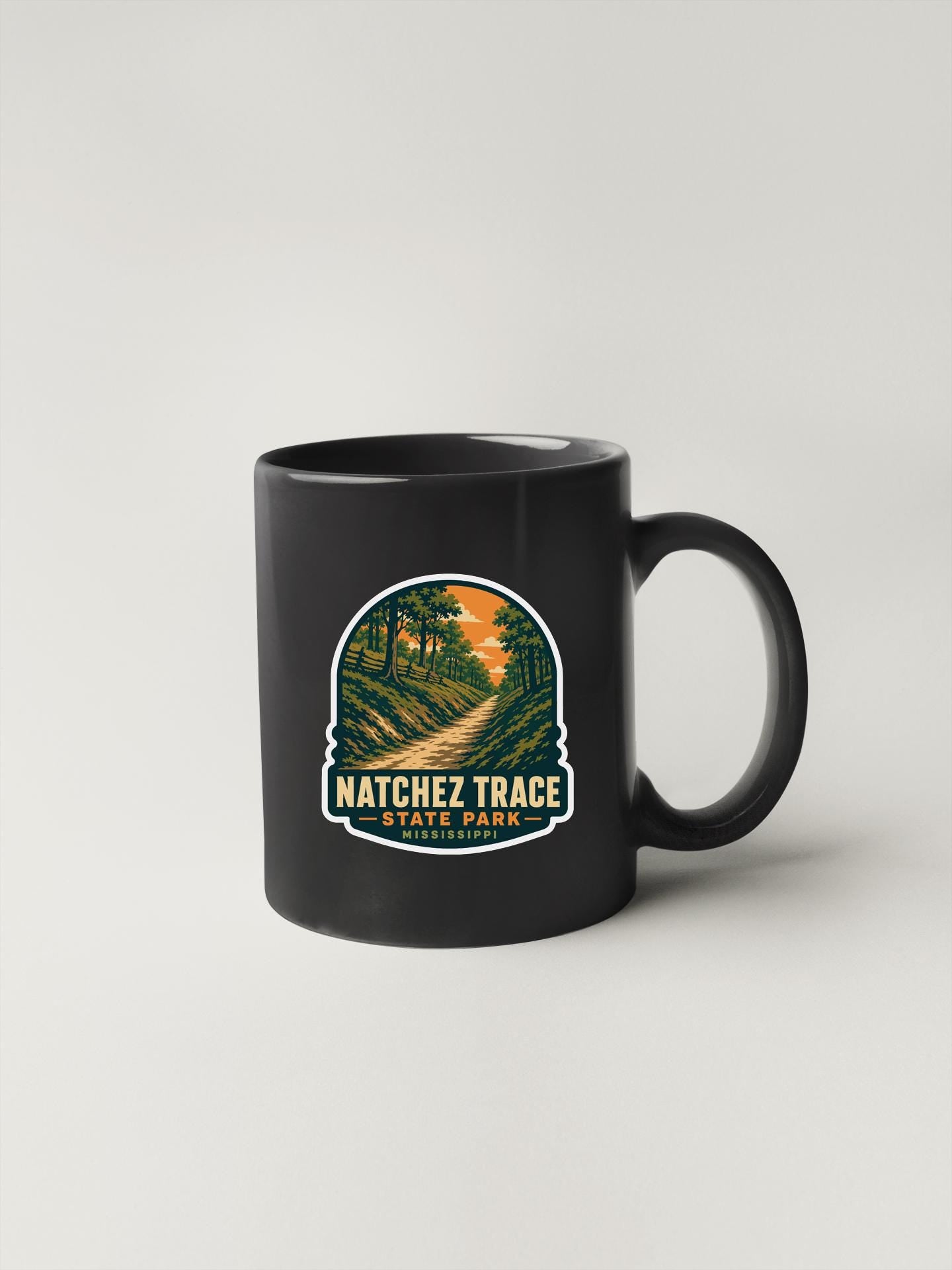 A black coffee mug with a graphic design depicting a scenic trail in a forested area.