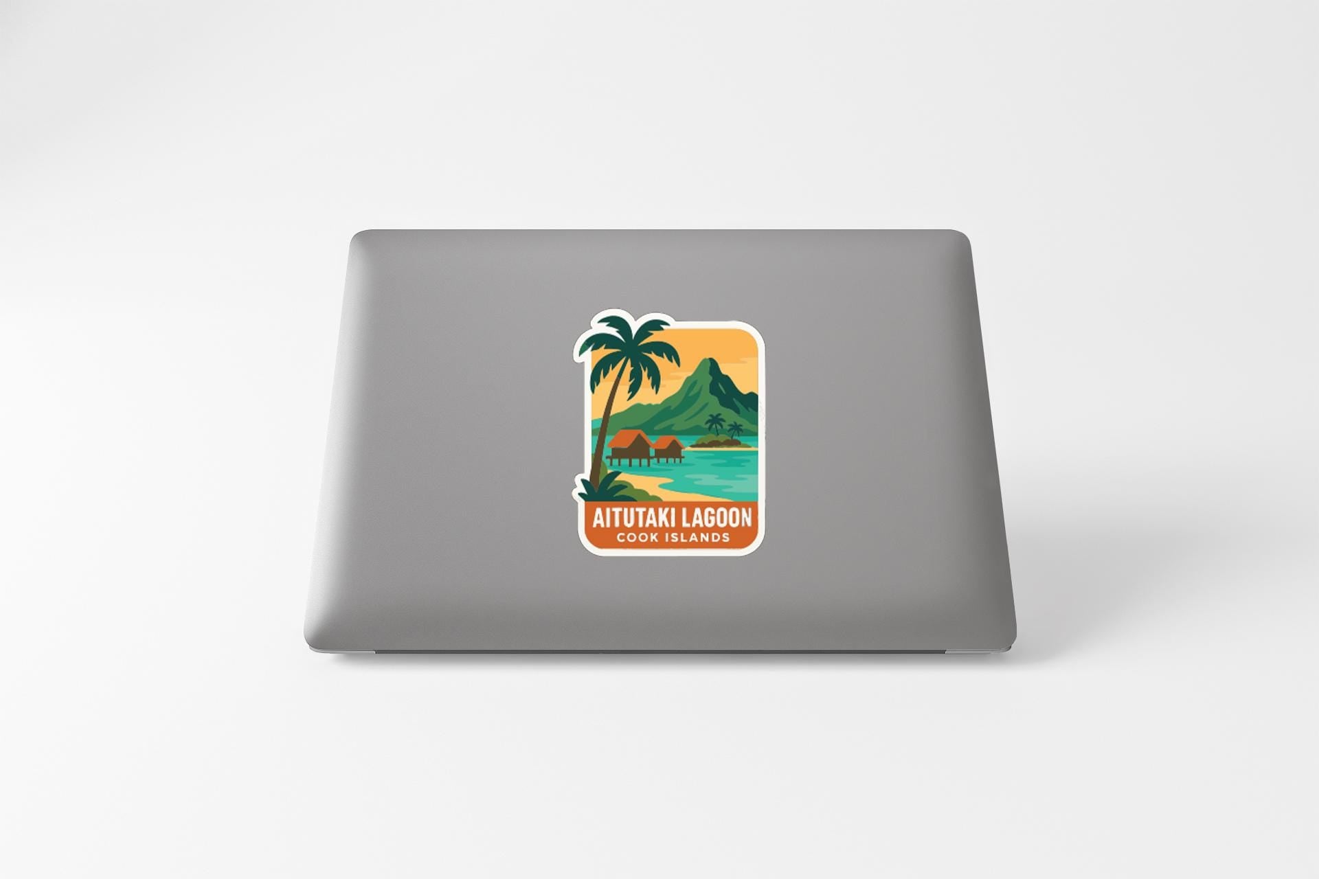 a sticker on the back of a laptop that depicts a tropical island scene with palm trees, mountains, and a body of water.