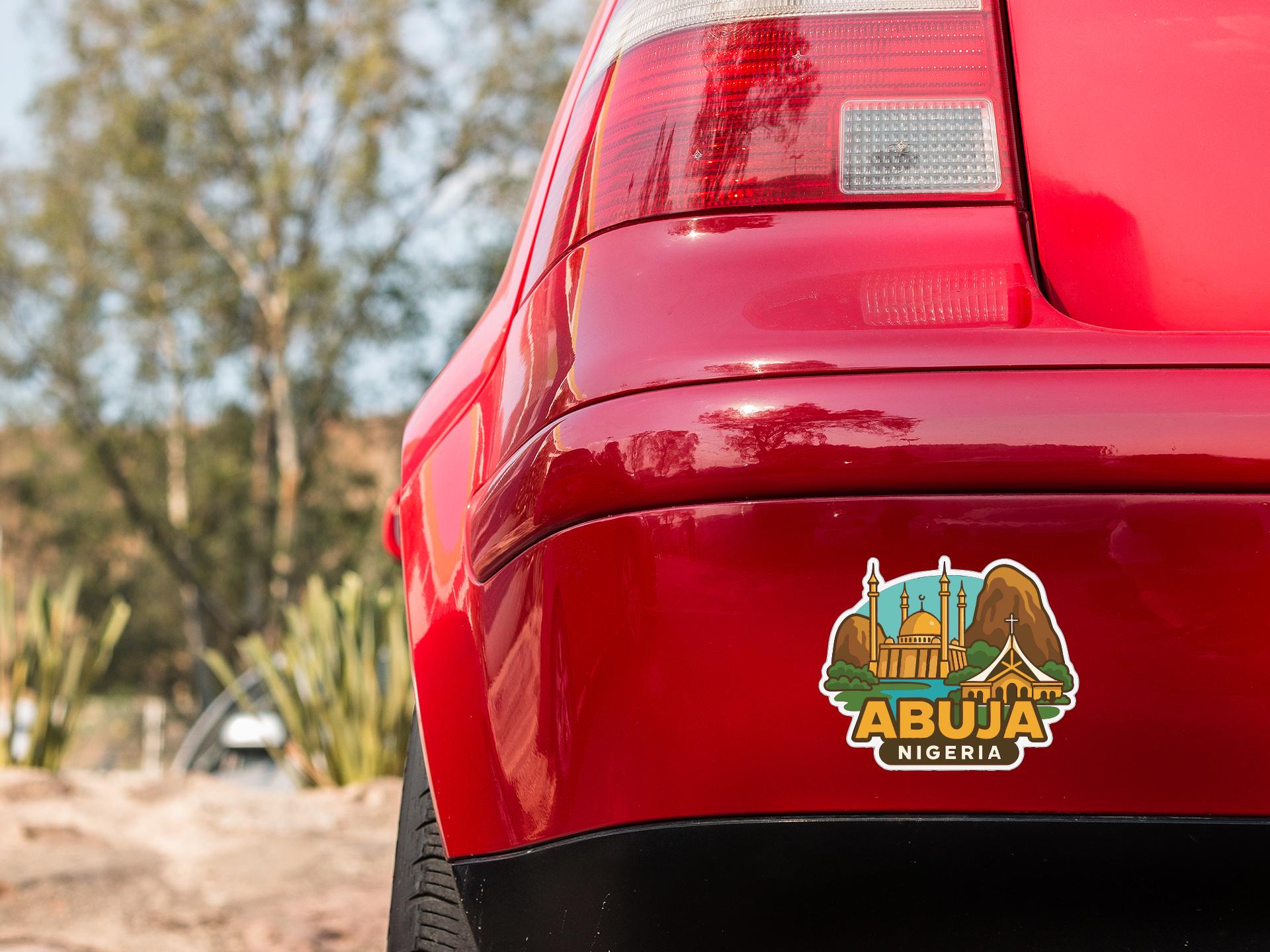 the rear end of a red car with a sticker on the trunk that features an illustration of Abuja, Nigeria.
