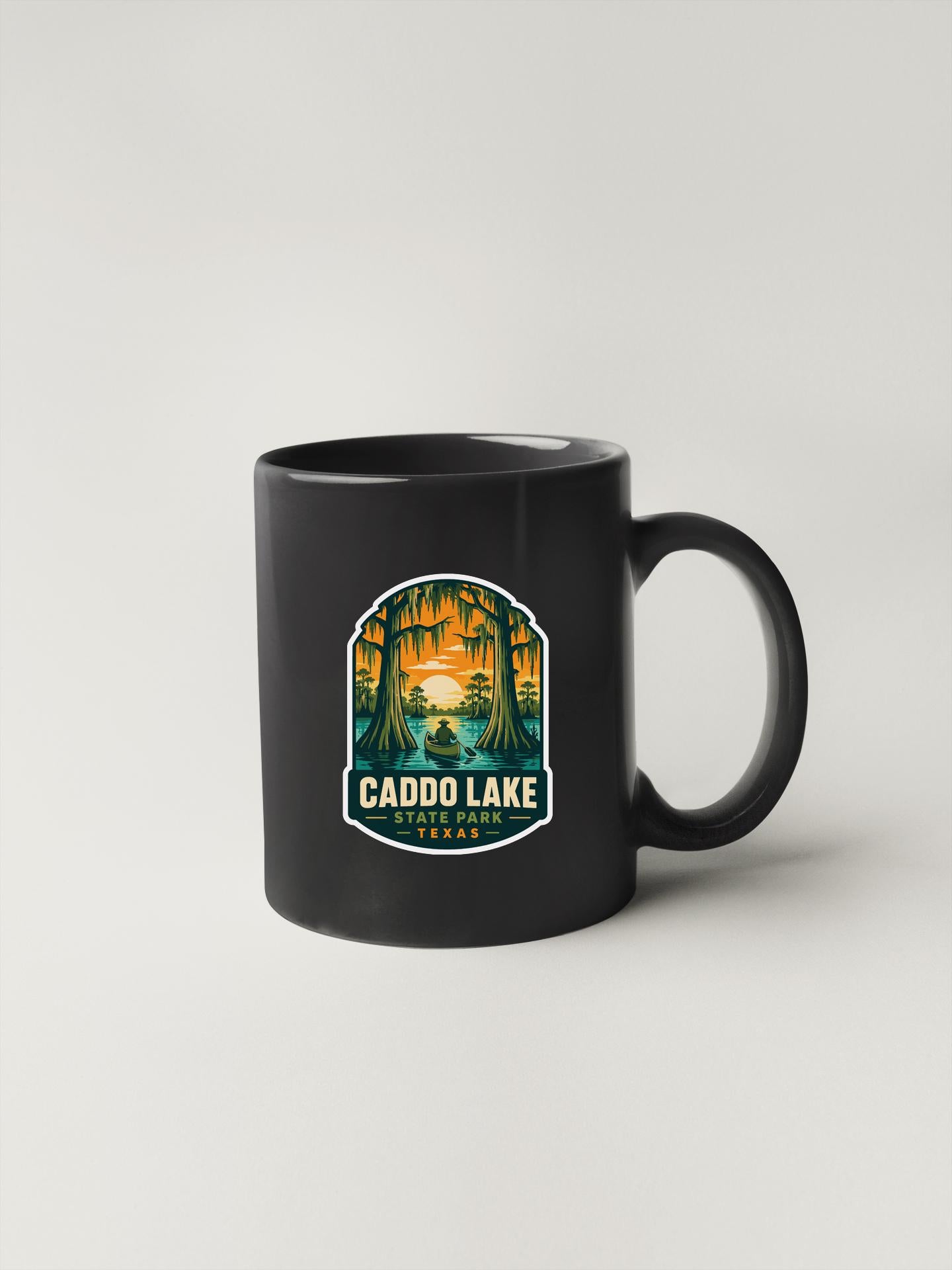 A black coffee mug with a sticker depicting a scenic landscape featuring a lake and trees.