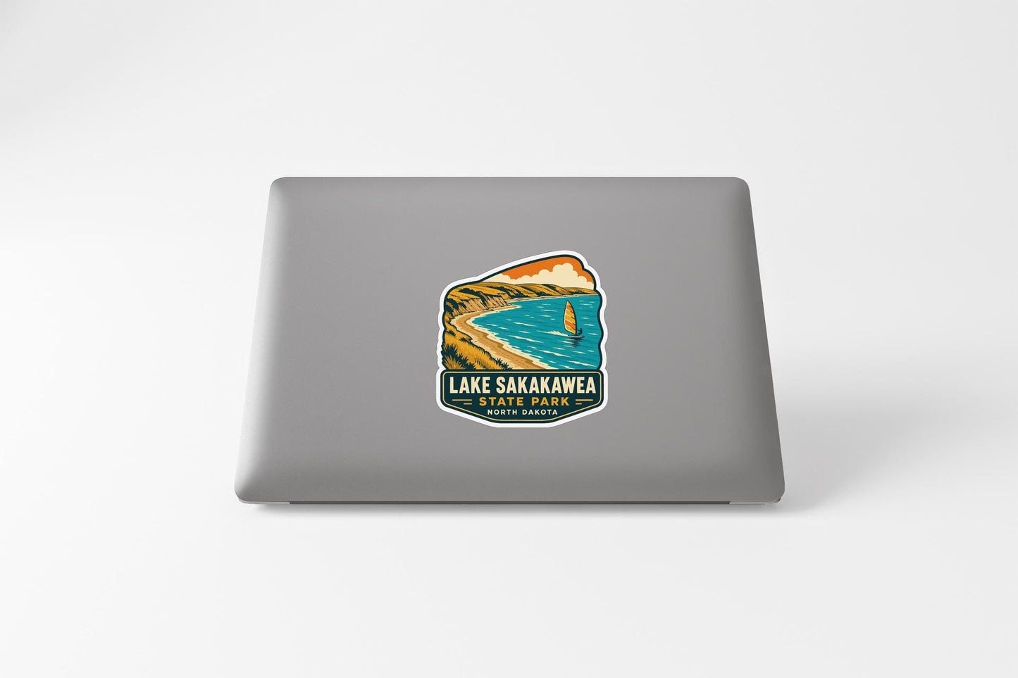 A sticker on the back of a laptop, depicting a scenic landscape with a lake, mountains, and a sailboat.