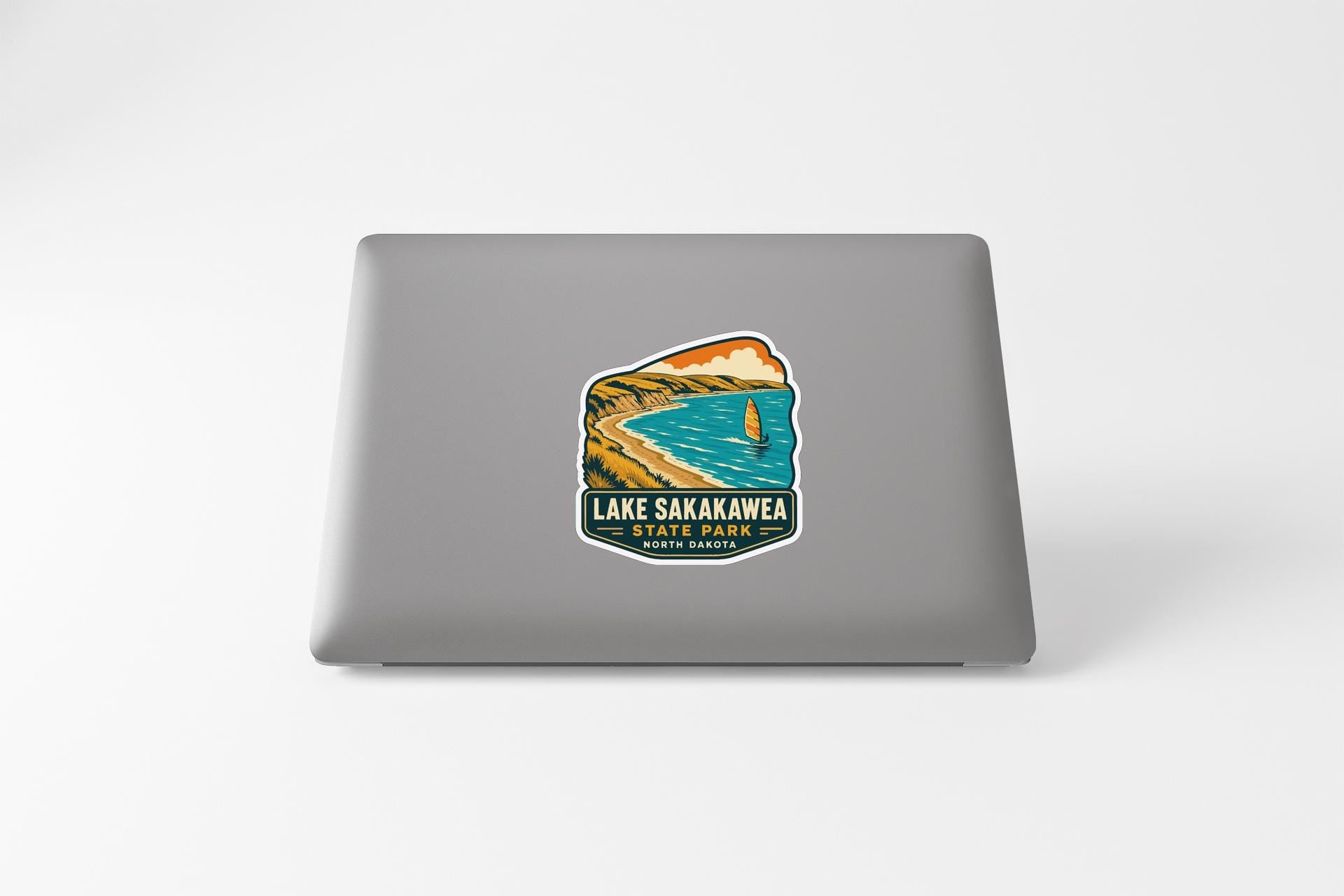 A sticker on the back of a laptop, depicting a scenic landscape with a lake, mountains, and a sailboat.