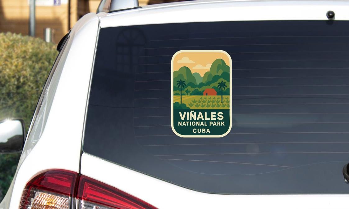 A sticker on the rear window of a white car, depicting a scenic landscape with mountains, palm trees, and a small building.