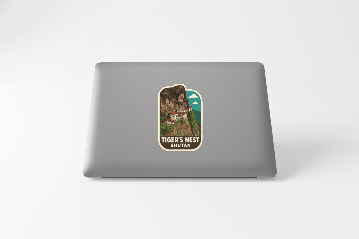 A sticker on the back of a laptop, depicting a scenic landscape with a mountain and a building, along with the text "TIGER'S NEST BHUTAN".