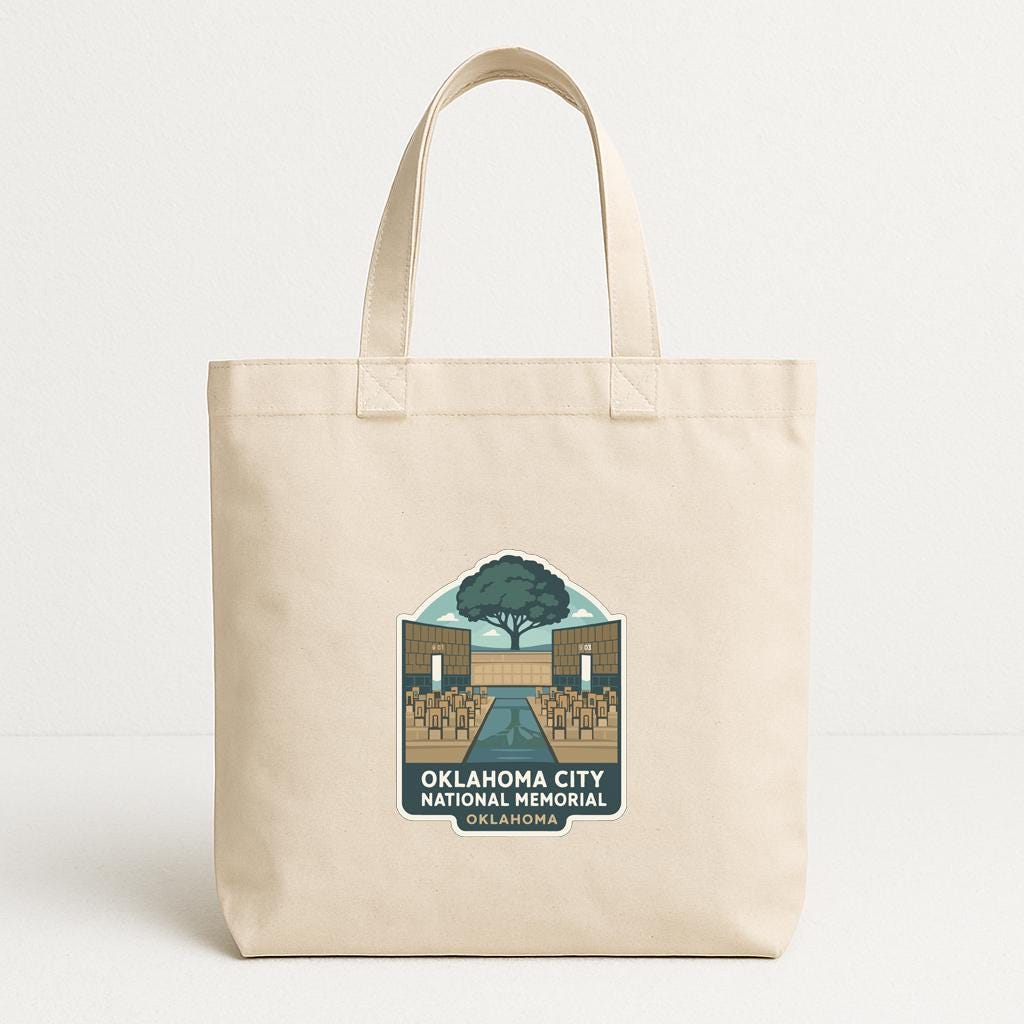 A beige tote bag with a graphic design featuring a tree and a building, along with text that reads "OKLAHOMA CITY NATIONAL MEMORIAL OKLAHOMA".