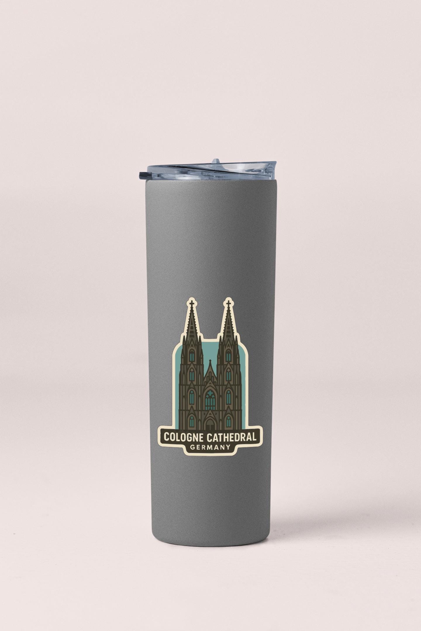A gray tumbler with a sticker depicting the Cologne Cathedral in Germany.