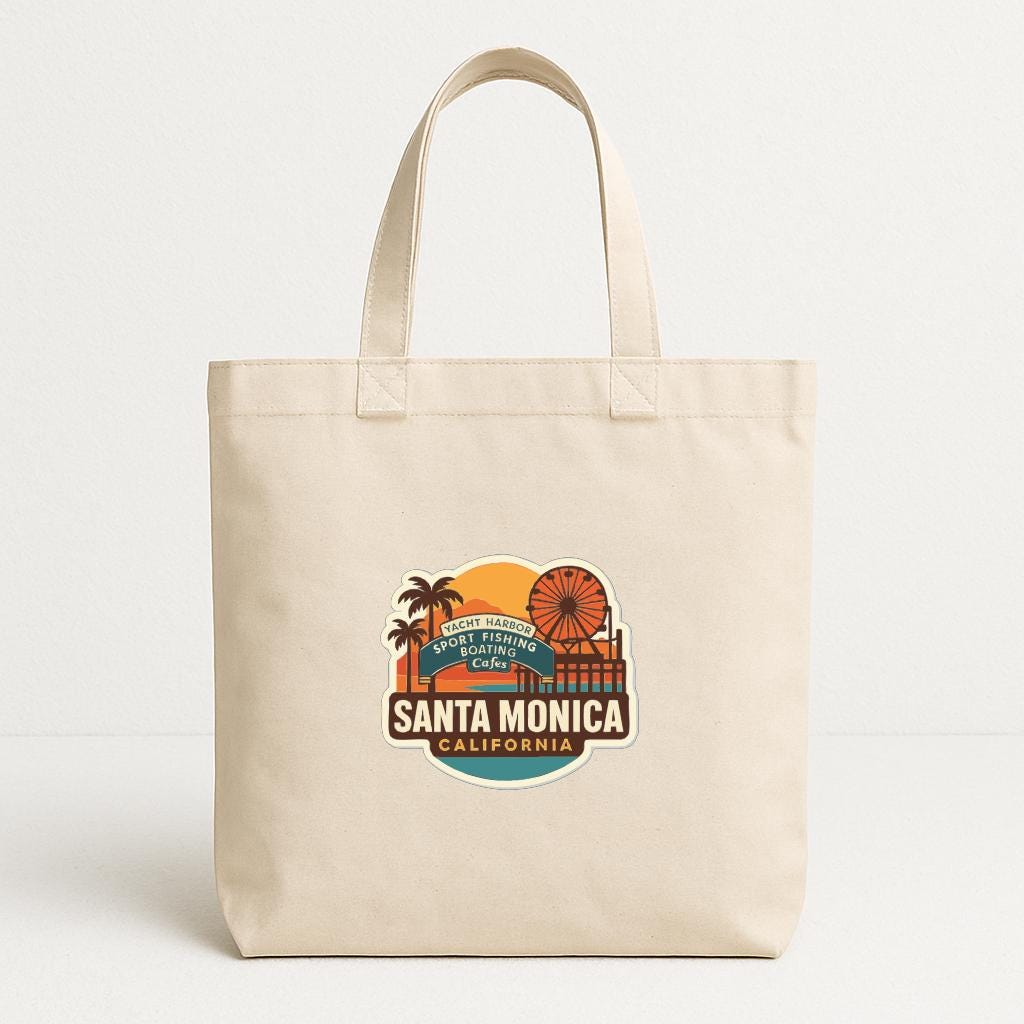 A beige tote bag with a graphic design featuring the text "SANTA MONICA, CALIFORNIA" and various icons, including a ferris wheel and palm trees, suggesting a beach or coastal theme.