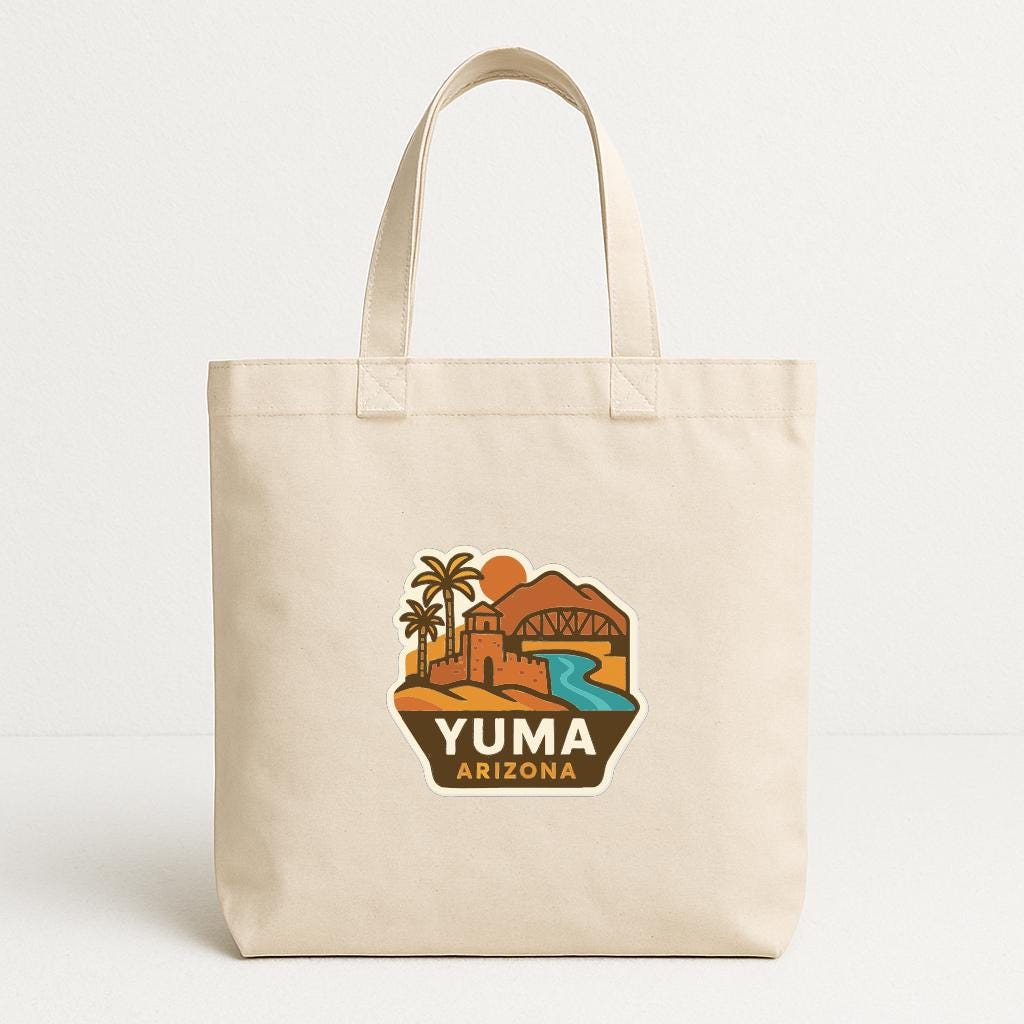 A beige tote bag with a graphic design depicting a desert landscape with a bridge, palm trees, and mountains, along with the text "YUMA ARIZONA".
