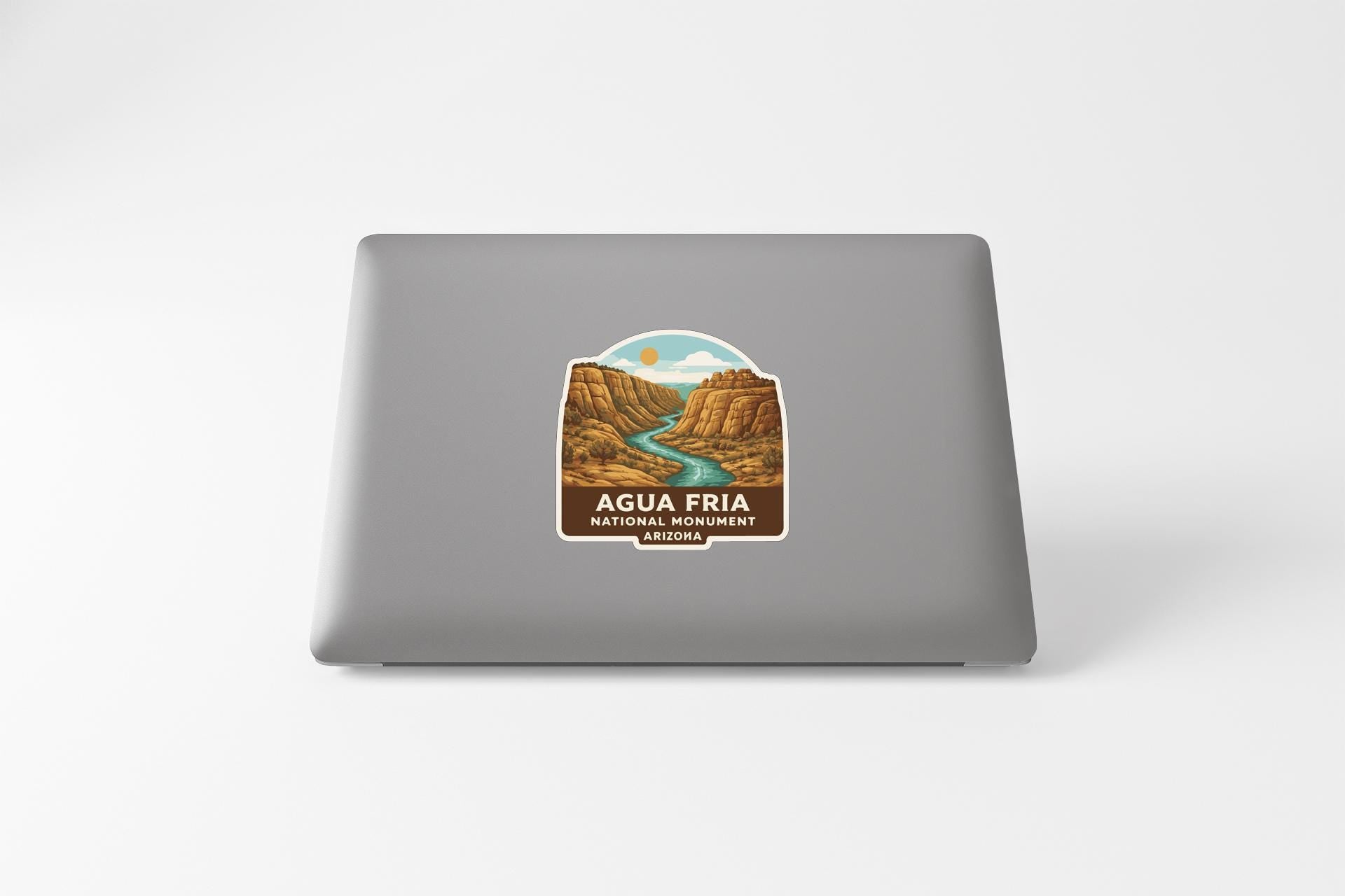 a sticker on the back of a laptop that displays a scenic landscape with a river and mountains.