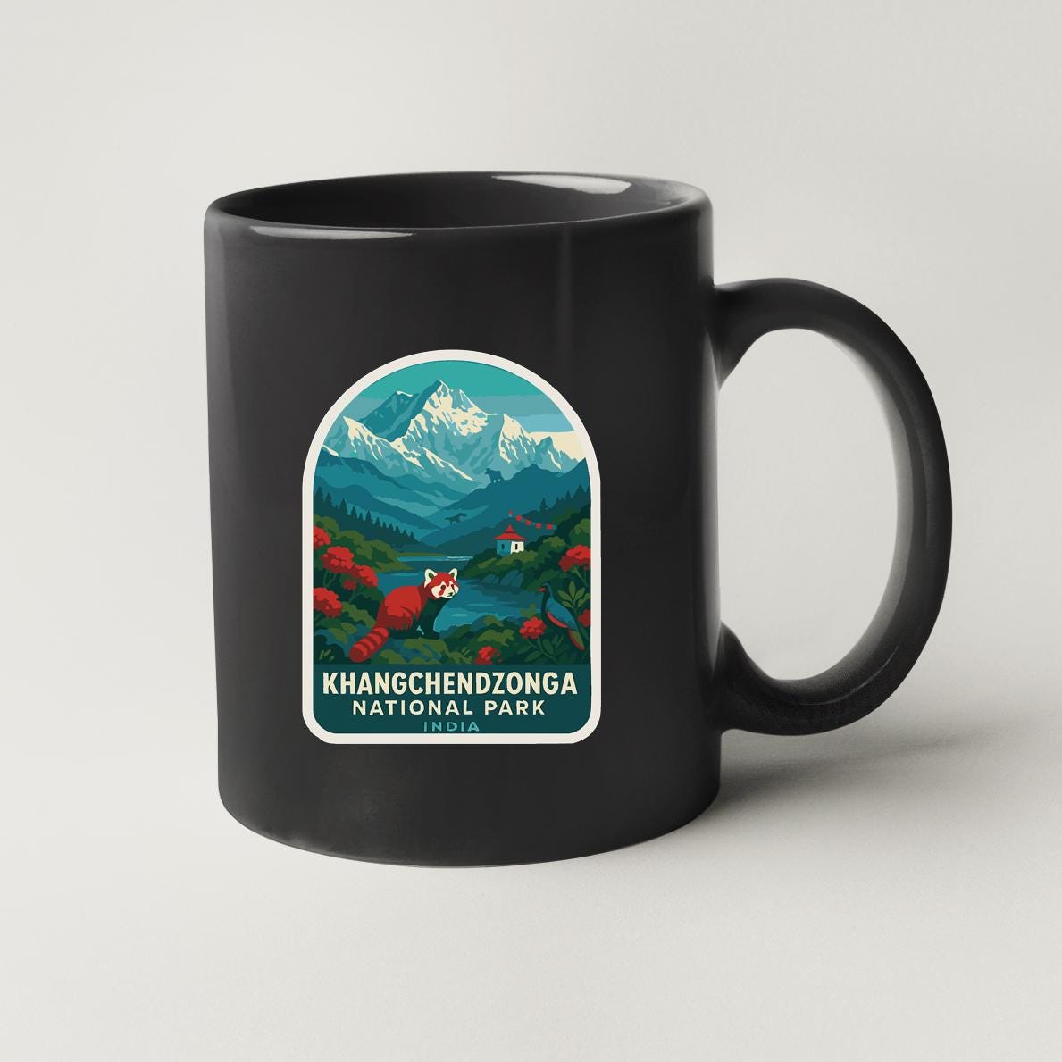 A black coffee mug with a graphic design depicting a mountainous landscape with a river and a small village.